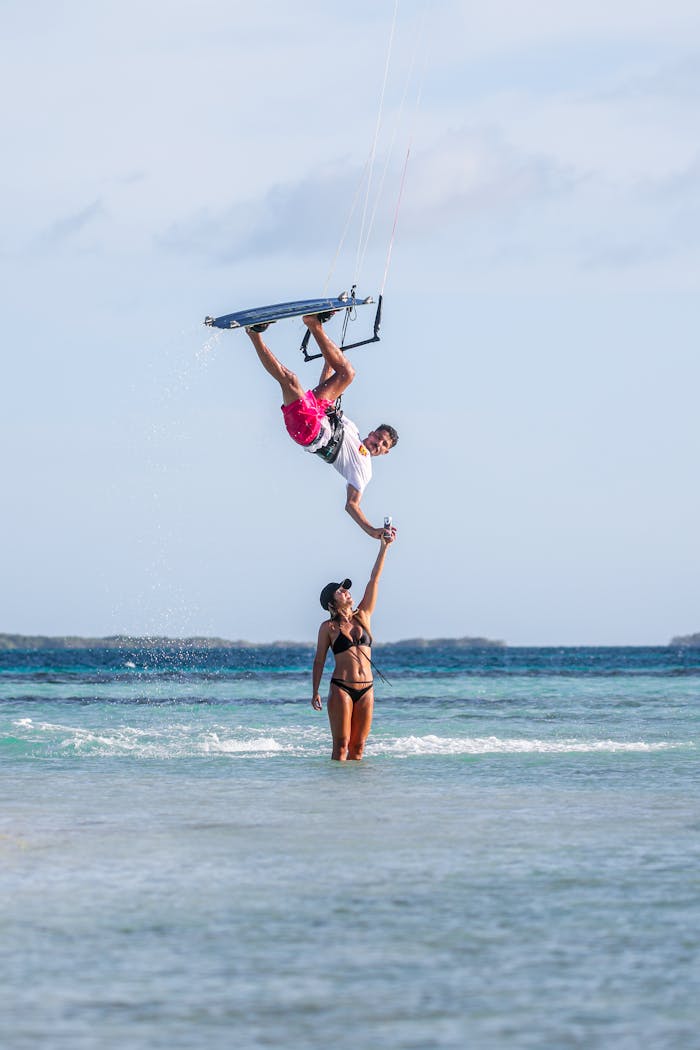why-choose-us A thrilling kitesurf jump executed by a man over calm ocean waters with a woman observing.