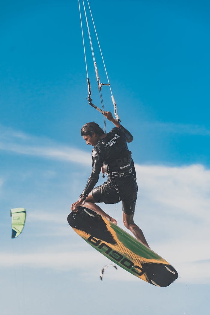 creative-02 Young man performing an impressive kitesurfing trick in midair against a clear blue sky.